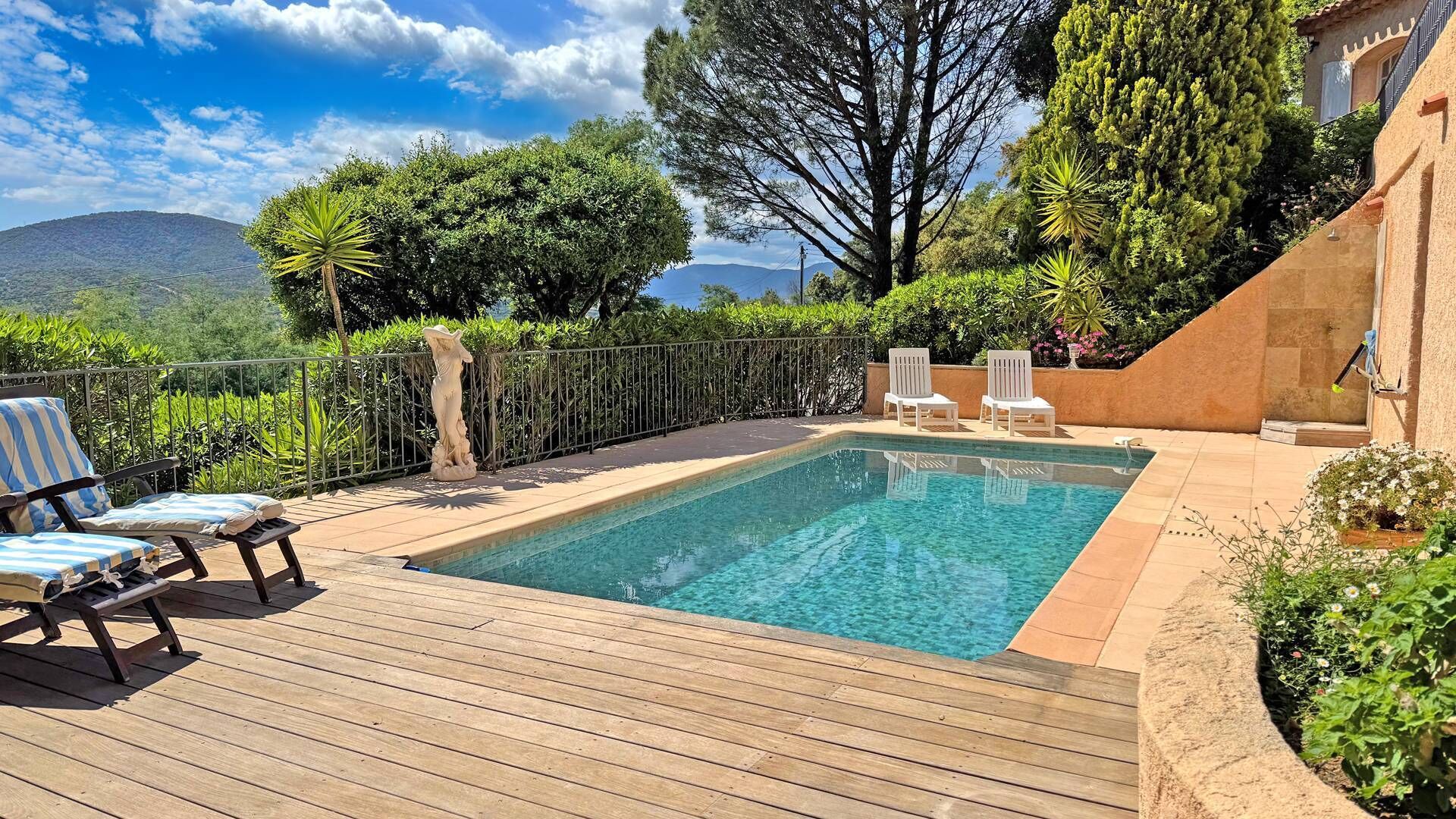 Une piscine rectangulaire dotée d’une terrasse en bois, entourée d’une clôture en métal et agrémentée de diverses plantes.