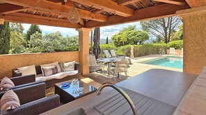 A covered outdoor area with a pool, wicker furniture, and a view of the surrounding landscape.