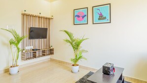 Una sala de estar moderna con un televisor de pantalla plana montado en una pared de paneles de madera, dos obras de arte enmarcadas y dos plantas en macetas.