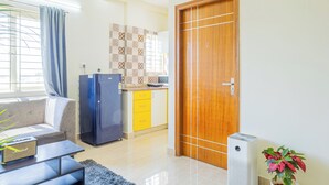 Una sala de estar con sofá, una mesita de centro, un refrigerador azul, un área de cocina con armarios amarillos y una puerta de madera.