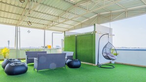 Un espacio al aire libre techado con césped artificial, mobiliario de mimbre y una silla colgante.