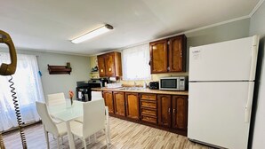 A compact kitchen with wooden cabinets, a microwave, a refrigerator, and a dining table with chairs. - Pet friendly Near Lake George and Saratoga (Corinth)