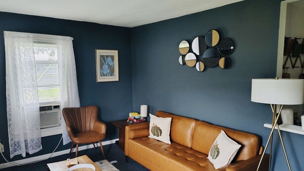 A living room with a brown leather sofa, a brown leather armchair, a white lamp, and a wall-mounted mirror. - Pet friendly Near Lake George and Saratoga (Corinth)