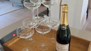 Un plateau en bois sur lequel sont disposés plusieurs verres à vin et une bouteille de champagne, le tout posé sur une table dans un salon moderne, avec un canapé et une fenêtre.
