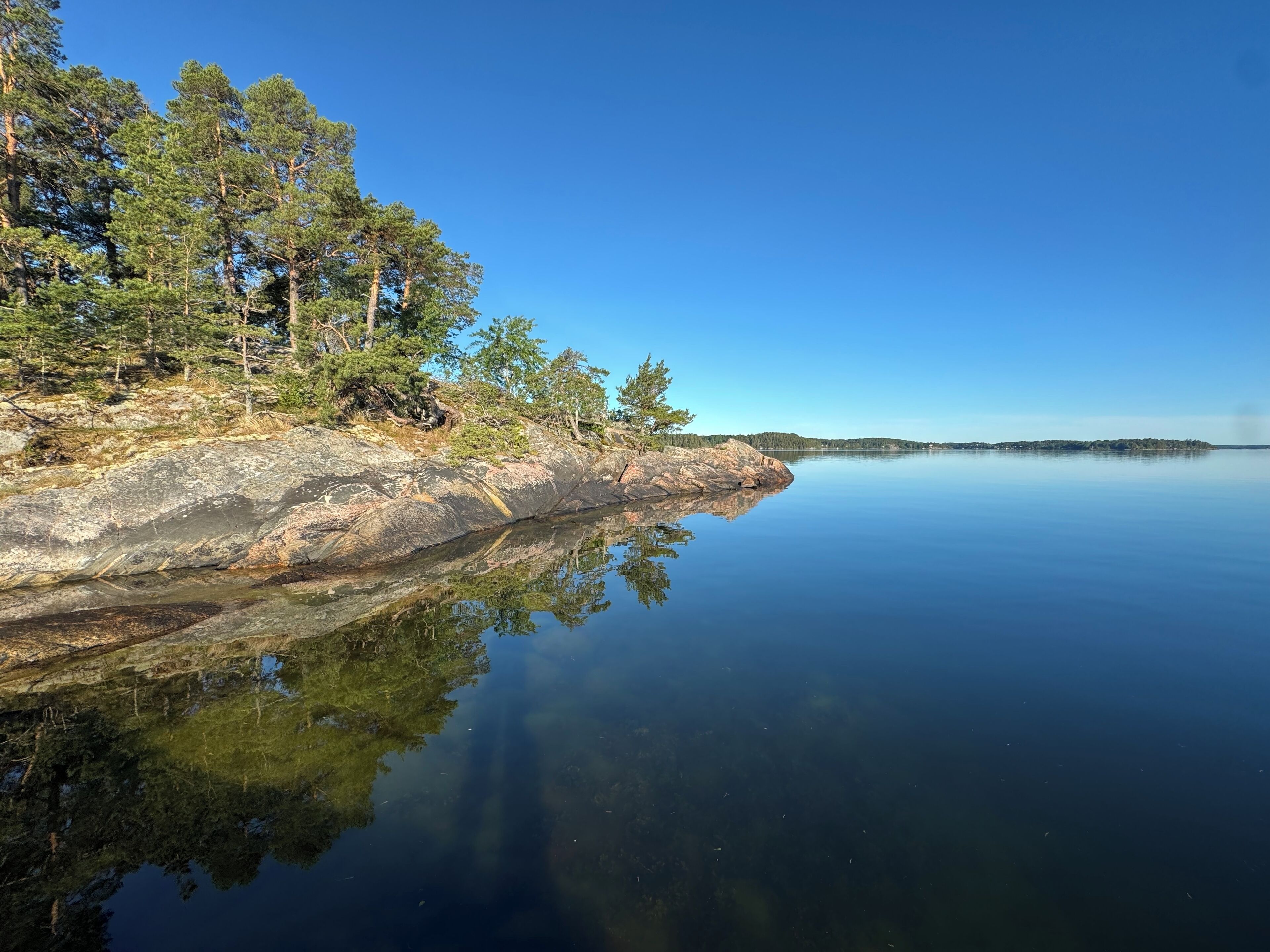 A calm lake with a rocky shoreline and trees reflecting on the water.