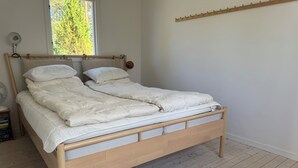 Un lit en bois avec une tête de lit, du linge de lit blanc et une fenêtre donnant sur des arbres.