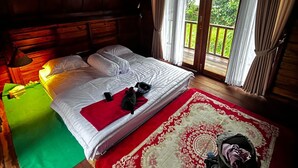 A wooden cabin bedroom with a bed, a green mat, a red and white patterned rug, and a suitcase on the floor. - Tetebatu rice field bliss (West Nusa Tenggara)