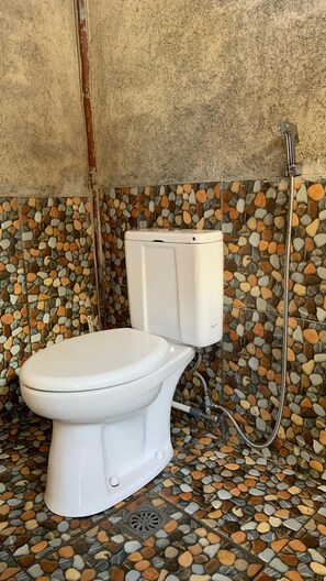 A toilet with a mosaic tile floor and a shower head. - Tetebatu rice field bliss (West Nusa Tenggara)