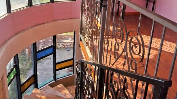 A room with a curved staircase, a dining area with a table and chairs, and large windows with a view of the outdoors.