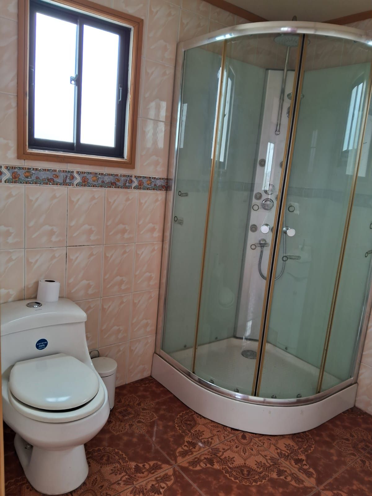 Une salle de bain comprenant des toilettes, une douche fermée par des parois de verre et une fenêtre située au-dessus des toilettes.