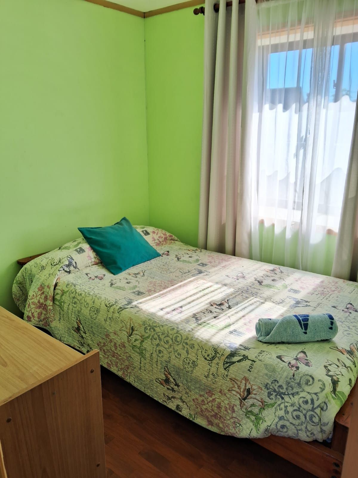 Een enkel bed met een bloemenbedekking, een blauwgroen kussen en een opgerolde handdoek op het bed.