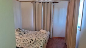 A bedroom with a bed, curtains, and a wooden floor.