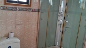 A bathroom with a toilet, a glass-enclosed shower, and a window above the toilet.