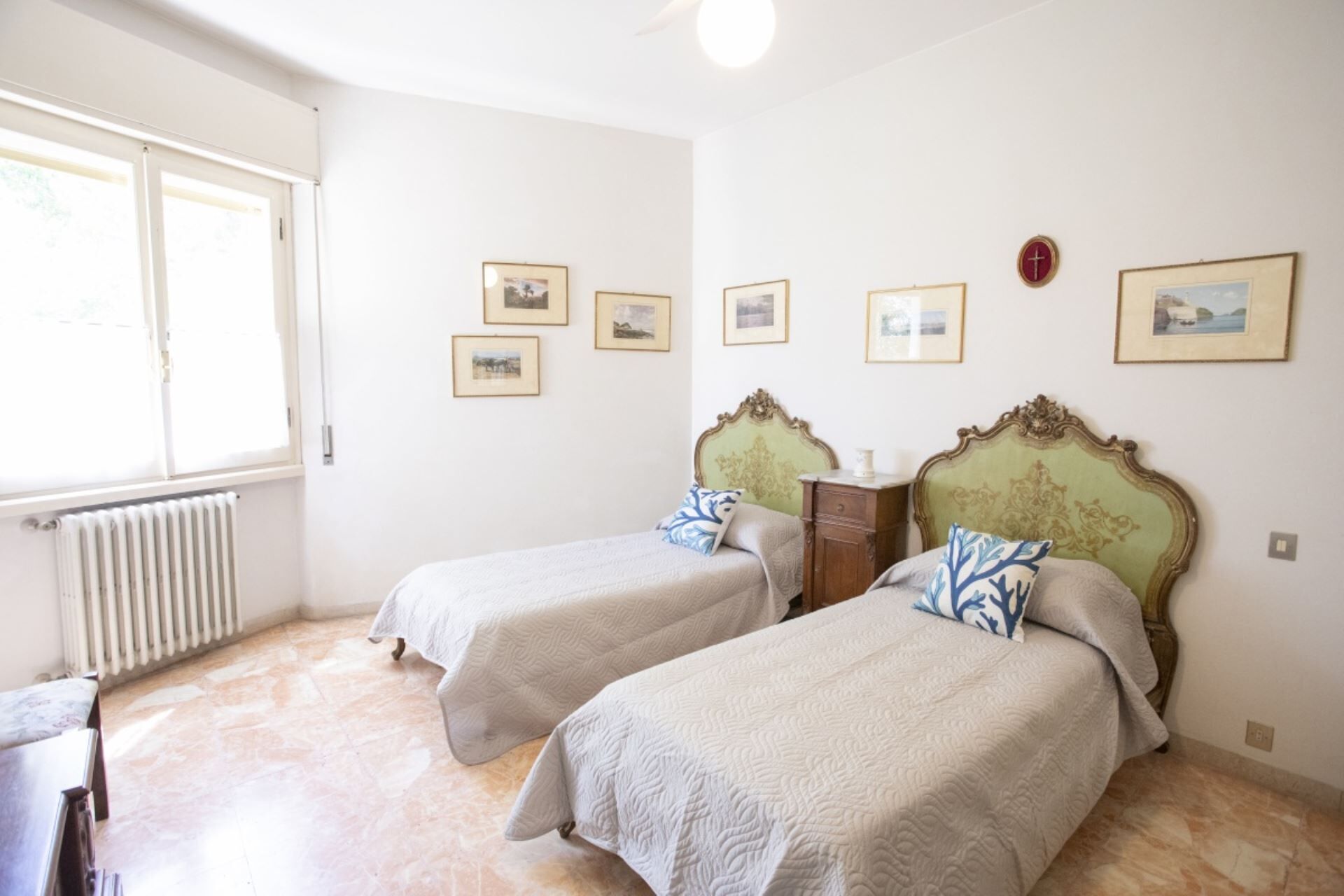 Una stanza con due letti, un termosifone e diverse foto incorniciate appese al muro.