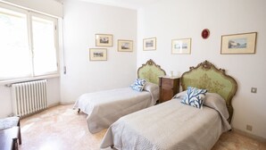 A room with two beds, a radiator, and several framed pictures on the wall.