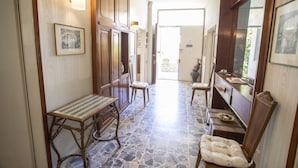 A hallway with a stone floor, wooden furniture, and framed pictures on the walls.