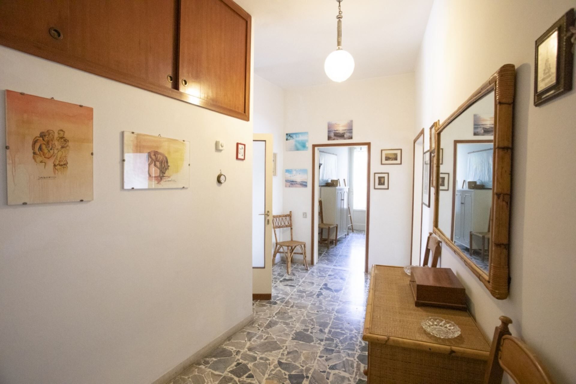 A hallway with stone flooring, wooden cabinets, and various framed artworks on the walls.