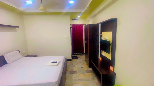 Habitación de hotel con cama, televisor montado en la pared y puerta que da a otra habitación.
