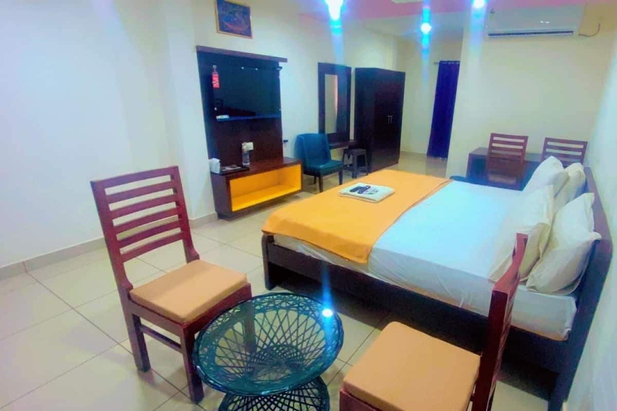 Una habitación de hotel con cama, una silla, una mesita, un armario y un espejo.