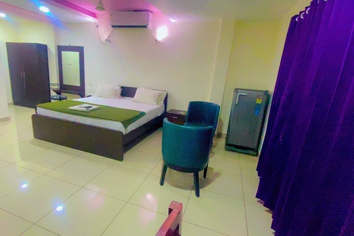 Habitación de hotel con cama, una silla, una mesita, un espejo y un refrigerador.