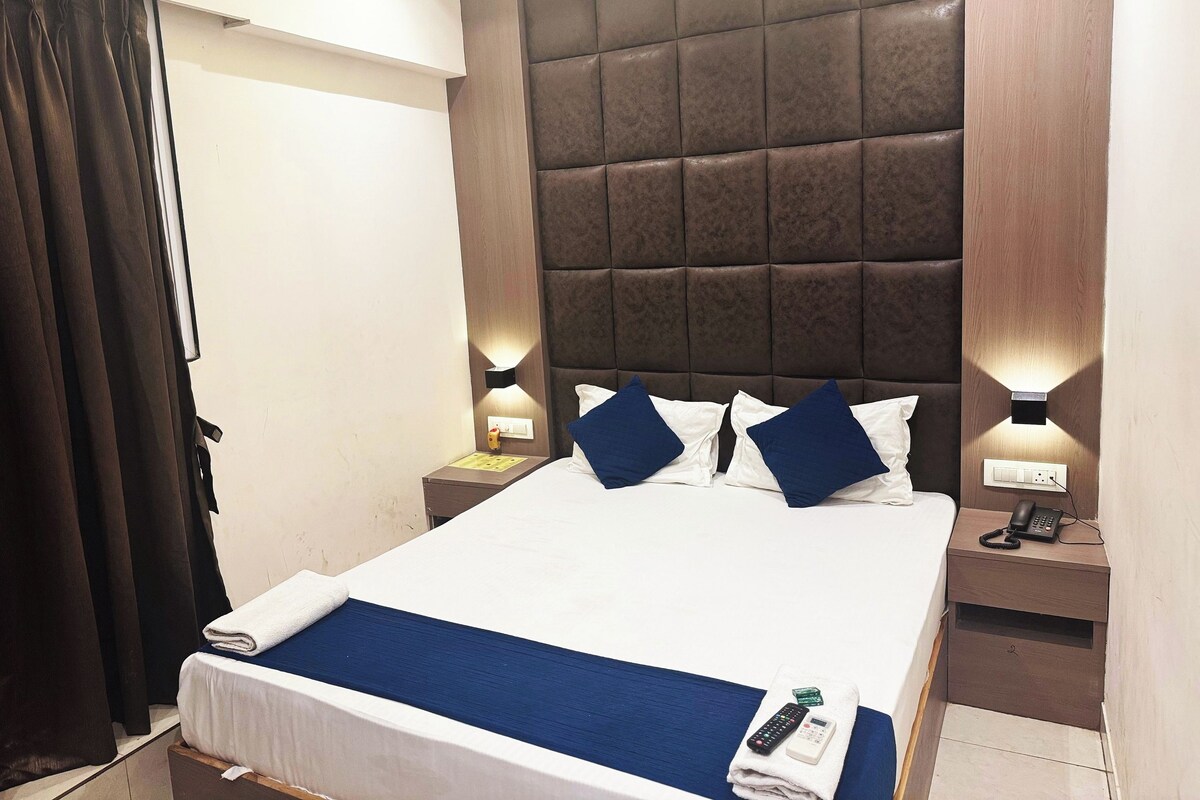 A hotel room with a large bed, a headboard, bedside lamps, a nightstand, and a curtain.