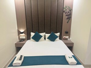 A hotel room with a large bed, two pillows, a bedside table with a lamp, a phone, and a remote control on the bed. - Hotel Sahara Residency (Mumbai)