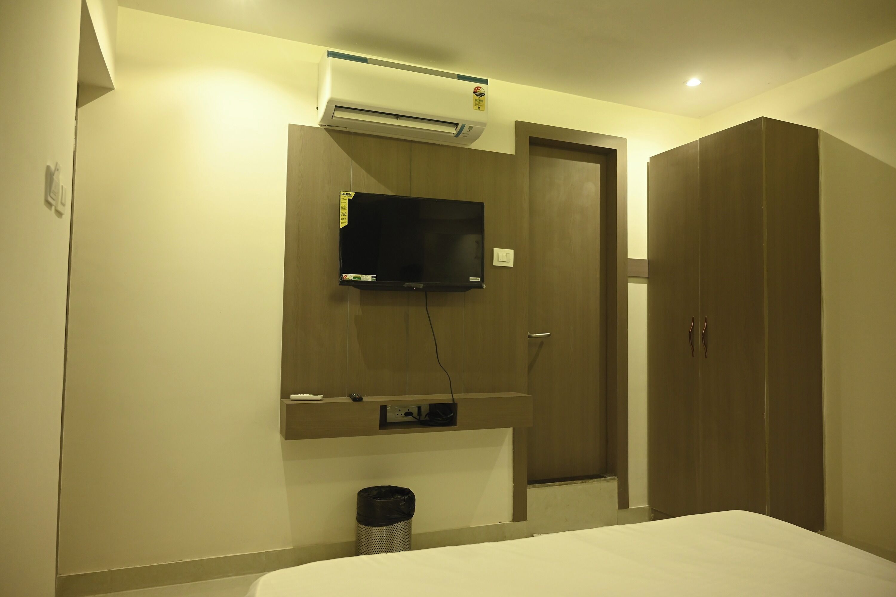 A hotel room with a bed, a TV mounted on the wall, a wardrobe, and an air conditioning unit.
