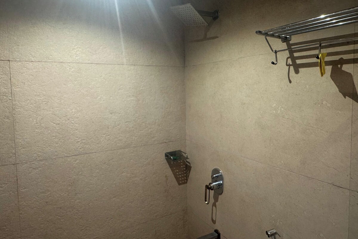 A small, dimly lit bathroom with a shower, a towel rack, and a wall-mounted towel dispenser.