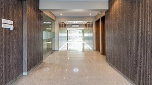 A modern hallway with wooden paneling, a glass door, and a sign indicating a room number. - Hotel Seven Oaks (Navi Mumbai)