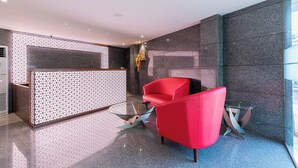 A modern reception area with a glass partition, a red armchair, and a small table. - Hotel Seven Oaks (Navi Mumbai)
