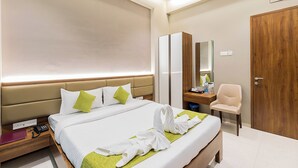 A hotel room with a large bed, a wooden wardrobe, a desk with a chair, and a mirror. - Hotel Seven Oaks (Navi Mumbai)