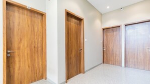 A hallway with three wooden doors, each marked with a number. The floor is covered with a light-colored carpet. - Hotel Seven Oaks (Navi Mumbai)