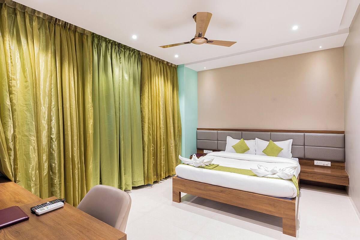 A hotel room with a bed, a desk, a chair, a nightstand, and a ceiling fan.