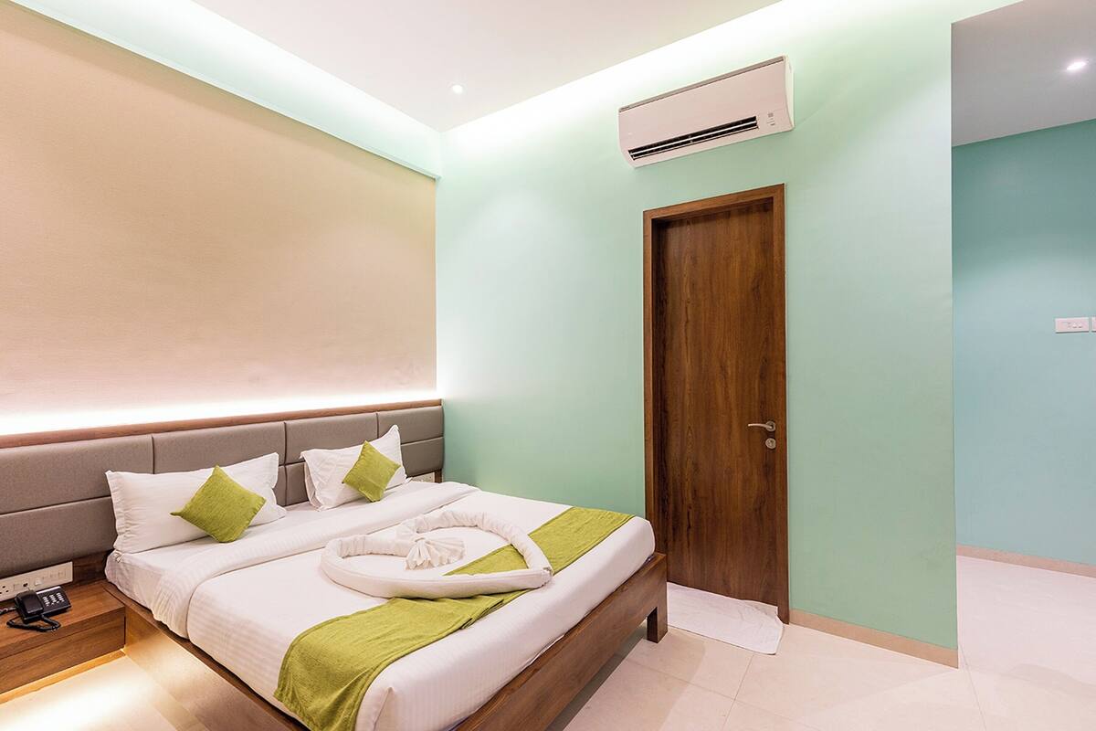 A modern hotel room with a neatly made bed, a wooden door, and an air conditioning unit on the wall.
