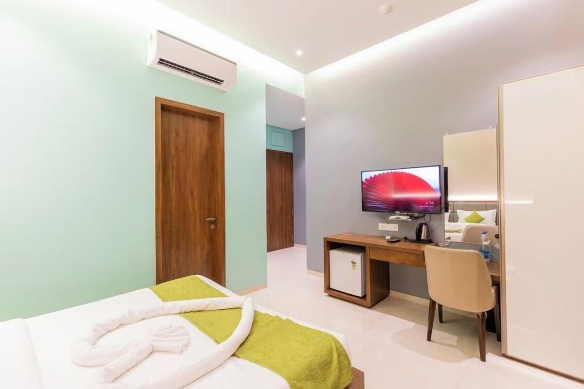 A hotel room with a bed, a desk with a computer, a television, and an air conditioning unit.