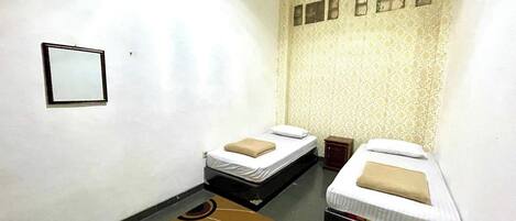A small, clean room with two single beds, a small table, and a patterned rug.