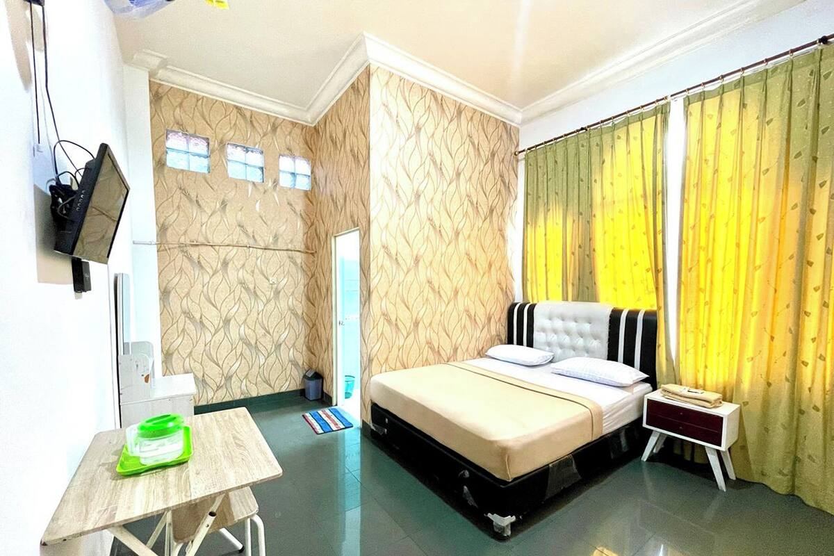 A hotel room with a bed, bedside table, and a TV mounted on the wall.