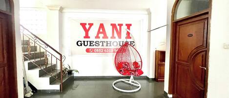 Un pasillo con una escalera, un sillón colgante rojo y un letrero que dice 'YANI GUESTHOUSE' con un número de teléfono.