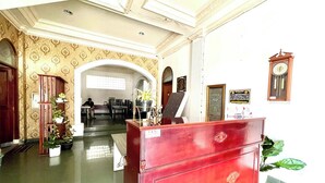 A reception area with a red counter, potted plants, and a clock on the wall. - Yani Guesthouse (Bukittinggi)