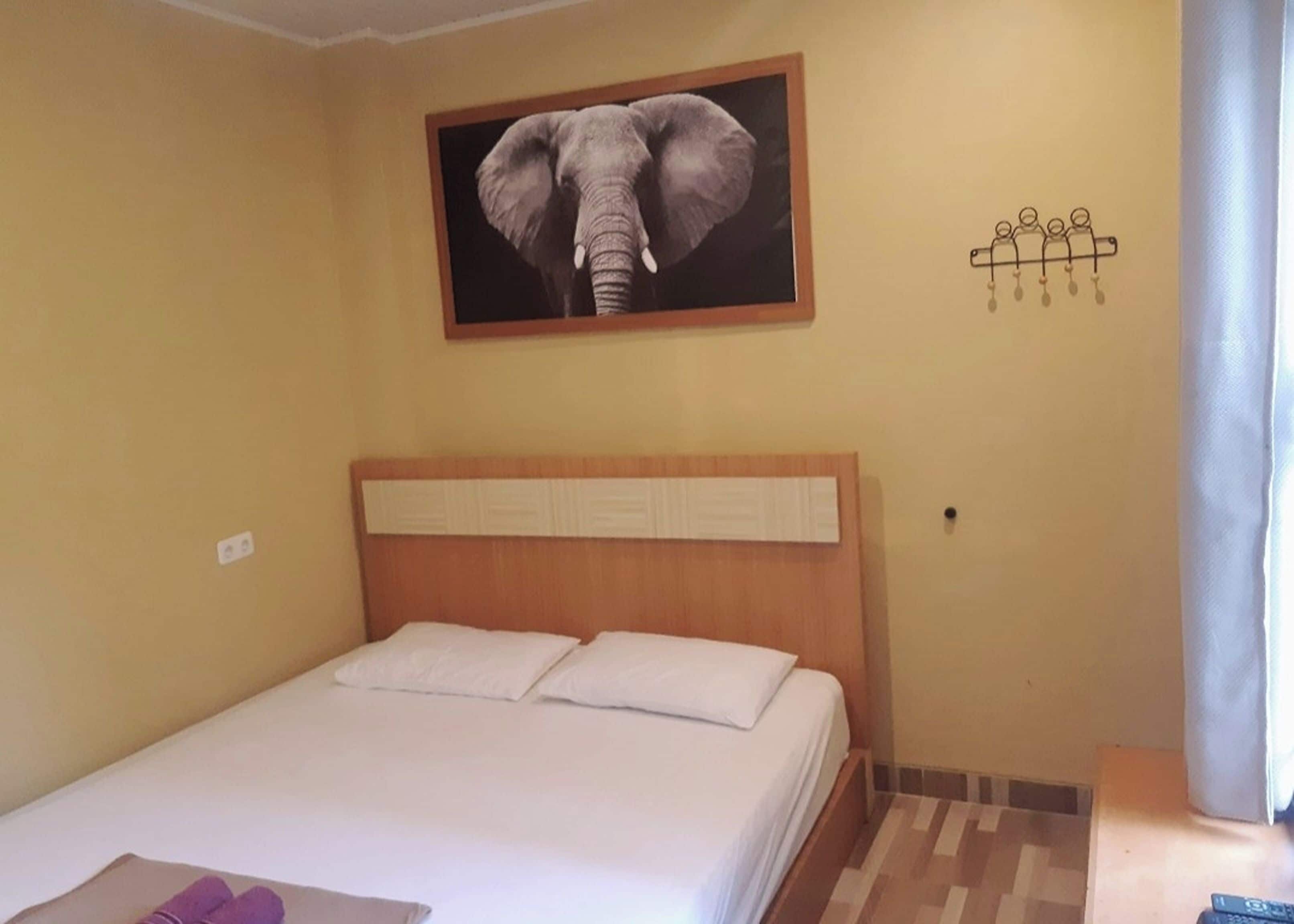 Habitación de hotel con una cama, un cabecero, un cuadro de un elefante colgado en la pared y una decoración mural con figuras humanas.