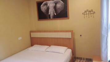 Habitación de hotel con una cama, un cabecero, un cuadro de un elefante colgado en la pared y una decoración mural con figuras humanas.