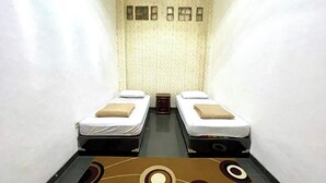A narrow room with two single beds, a patterned wall, and a carpet with circular designs. - Yani Guesthouse (Bukittinggi)