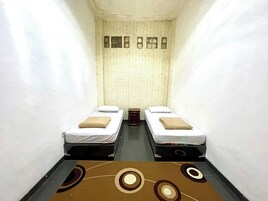 A narrow room with two single beds, a patterned wall, and a carpet with circular designs.