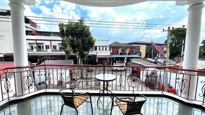 A balcony with two wicker chairs and a small table, overlooking a street with buildings and a tree. - Yani Guesthouse (Bukittinggi)
