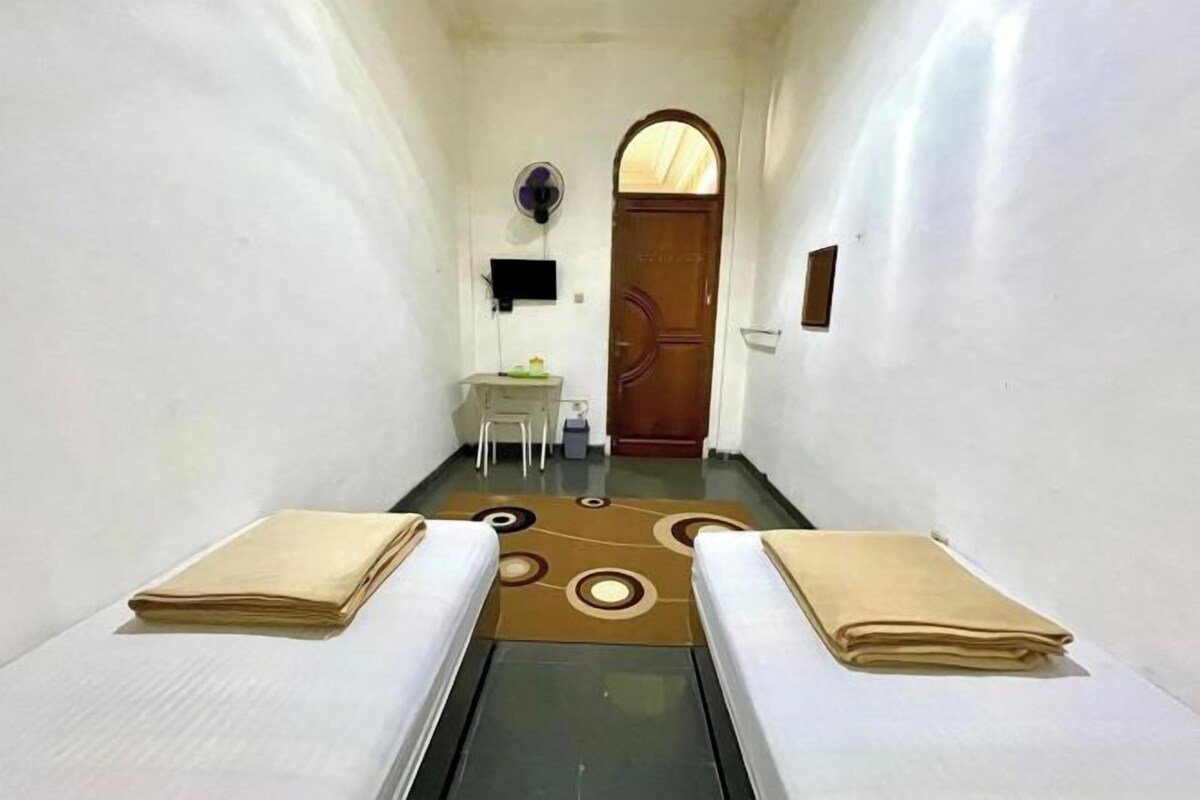 A narrow hallway with two beds, a desk, and a door at the end.