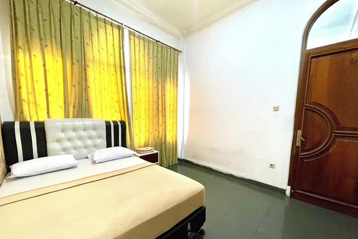 A hotel room with a bed, curtains, a wooden door, and a tiled floor.