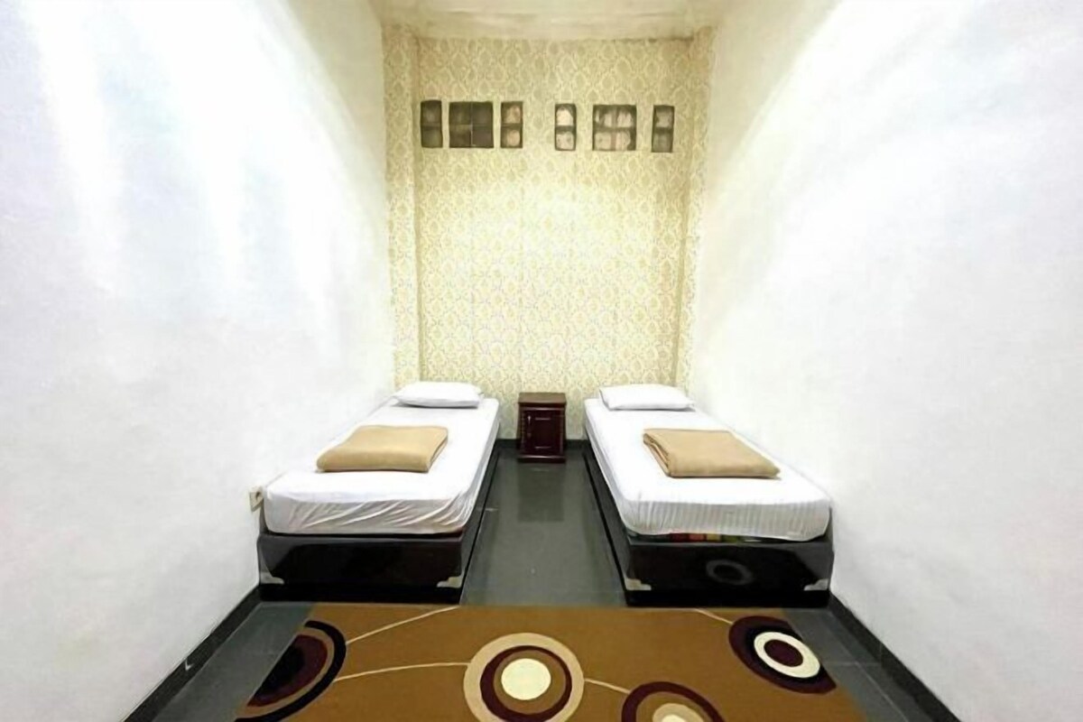 Quarto pequeno e estreito com duas camas de solteiro, parede estampada e tapete com desenhos circulares.