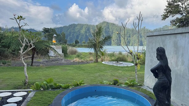A swimming pool with a statue, surrounded by a well-maintained lawn and a view of a lake and mountains. - Green Lake Bali (Kintamani)