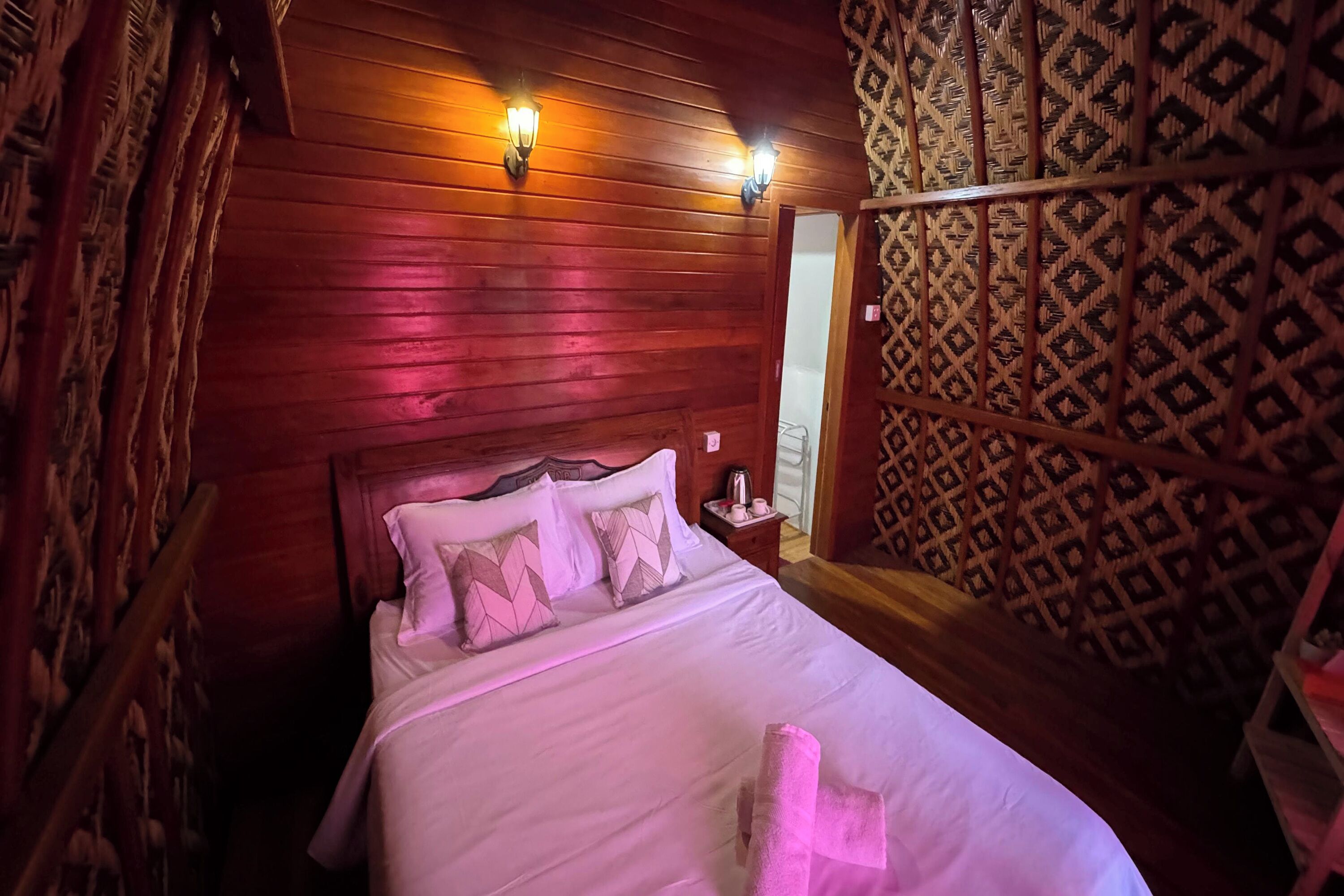 A wooden-paneled room with a bed, two wall-mounted lights, and a patterned wall.