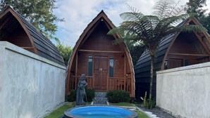 A wooden cabin with a swimming pool, surrounded by a garden and a statue. - Green Lake Bali (Kintamani)